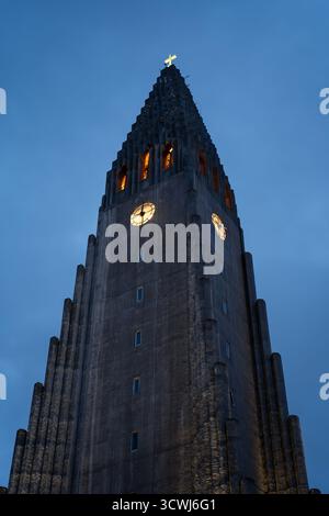 L'église Hallgrimskirkja à Reykjavik, Islande, avec sa façade en gradins et sa flèche lumineuse, se dresse contre un ciel frais du soir. Banque D'Images