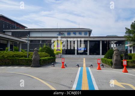 Le Centre des arts provinciaux de Jeju fait face à un parvis flanqué de statues de dol hareubang, avec des bannières et des panneaux sur la façade moderne revêtue de basalte. Banque D'Images