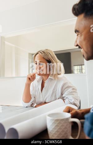 Une femme d'âge moyen et un jeune homme, discutant de plans architecturaux, dans un cadre de bureau moderne, faisant preuve de travail d'équipe et de créativité. Banque D'Images