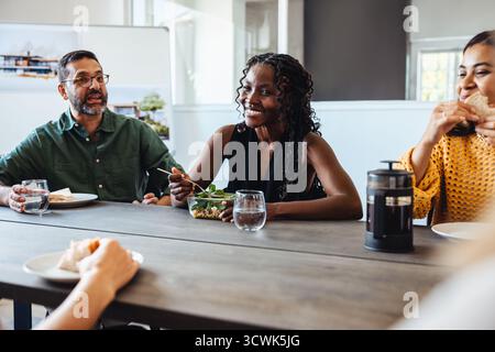 Un groupe diversifié de jeunes professionnels et d’âge moyen partagent une pause déjeuner lors d’une réunion d’équipe dans une petite firme d’architecture. Travail d'équipe, collaboration Banque D'Images