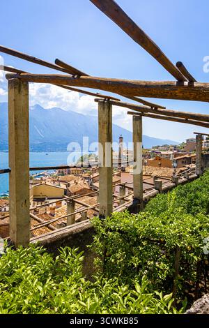 Charmante vue sur le clocher historique de Limone sul Garda avec les Alpes en arrière-plan et des fleurs floues colorées au premier plan. Idéal pour les voyages, Banque D'Images