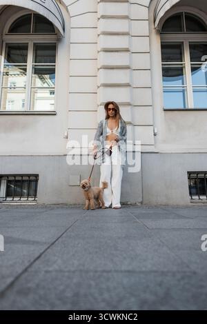 Femme promenant son caniche mignon en laisse dans la ville. Vue arrière de la tenue élégante, promenade estivale détendue dans un cadre urbain. PET Care, Lifestyle et Fa Banque D'Images