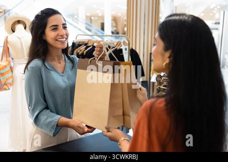 Client latin positif prenant des sacs à provisions en papier de l'assistant commercial Banque D'Images