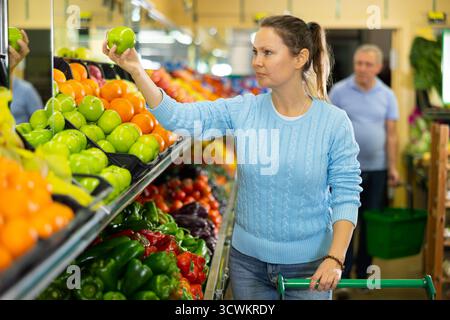 Une femme d'âge moyen achète des pommes fraîches à l'épicerie Banque D'Images