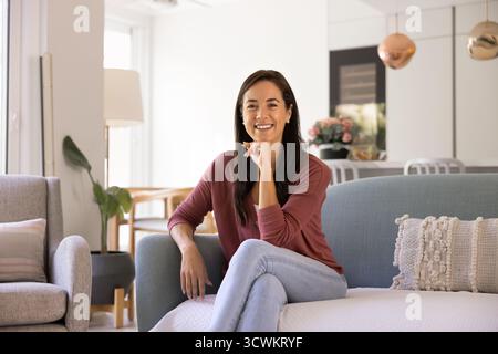 Heureuse femme propriétaire latine confiante assise sur le canapé Banque D'Images