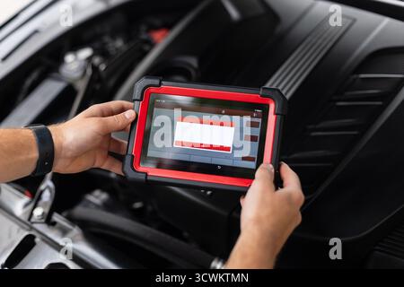 Gros plan d'Un technicien tenant un dispositif de diagnostic avancé à l'intérieur d'Une voiture et effectuant des vérifications du système. Entretien automobile moderne et Di électronique Banque D'Images
