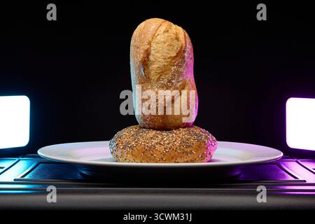 Composition verticale de deux petits pains empilés sur plaque avec un éclairage violet et cyan vif. Boulangerie minimaliste moderne nature morte. Banque D'Images