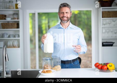 Homme des années 40 mange le petit déjeuner dans la cuisine. Guy aime la nourriture fraîche à la table de la cuisine le matin. Un homme mange des céréales et des fruits dans la cuisine. Man Banque D'Images