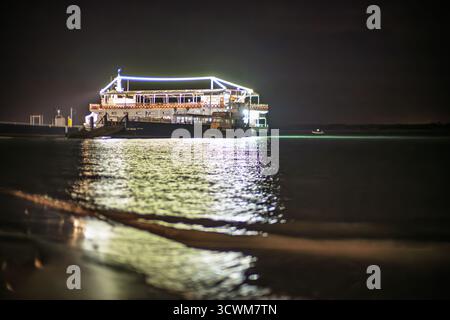 À Sanlucar de Barrameda, un bateau d'excursion scintille de lumières blanches et bleues, projetant des reflets sur le Guadalquivir sombre alors qu'il repose paisiblement à Nigh Banque D'Images