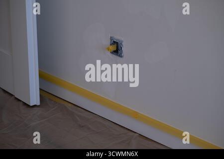 Gros plan du mur avec la prise électrique recouverte de ruban adhésif et de plaques de plâtre visibles. Chambre préparée pour rénovation et peinture. Concept de réparation à domicile Banque D'Images