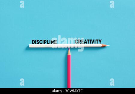 Crayon blanc équilibre sur un crayon rose représentant l'équilibre entre créativité et discipline sur un fond bleu éclatant Banque D'Images