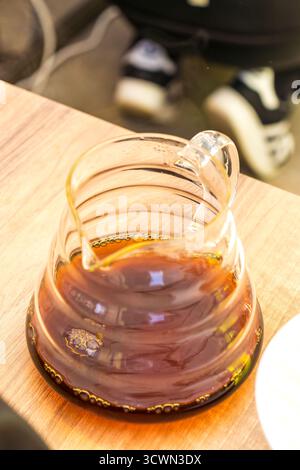 Café noir fraîchement infusé dans une carafe en verre sur une table en bois, gros plan du résultat de l'infusion. Banque D'Images