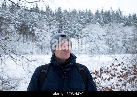 portrait d'homme mature en hiver avec forêt derrière couvert de neige, homme avec bonnet et veste d'hiver gros plan portrait, gens ordinaires Banque D'Images
