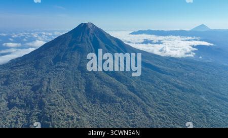 Le puissant cône d'un volcan domine l'horizon, entouré de nuages dérivants et de forêts sans fin, capturant l'essence sauvage du natur indonésien Banque D'Images