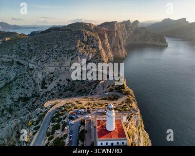Vue aérienne d'un phare blanc avec un toit rouge de garde debout sur les falaises rocheuses, où la route serpente à travers les montagnes, Cap de Formentor, Îles Baléares, Espagne. Banque D'Images