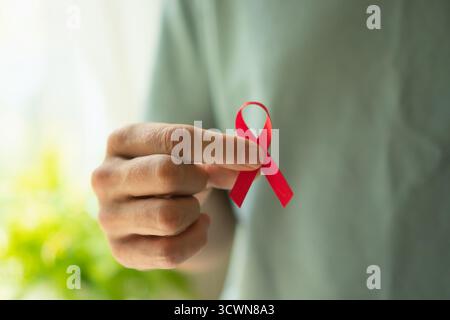 Gros plan d'une main masculine offrant un ruban de sensibilisation rouge représentant le soutien à la mémoire du VIH/sida et la solidarité médicale en décembre. Banque D'Images
