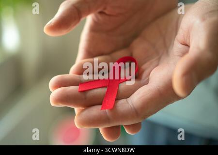 Gros plan des mains masculines s'ouvrant pour révéler un ruban de satin rouge sur la paume, symbolisant le soutien au VIH/sida, le souvenir et l'espoir d'une guérison future. Banque D'Images