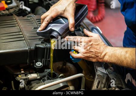 Mains de mécanicien versant de l'huile moteur d'une bouteille dans un moteur de voiture Banque D'Images
