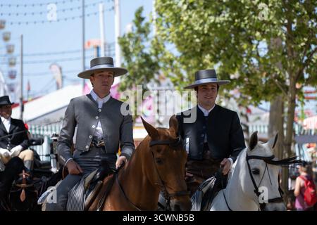 Sevilla, Espagne - 23 avril 23 : deux hommes en tenue traditionnelle à cheval à une foire, avec un fond festif Banque D'Images