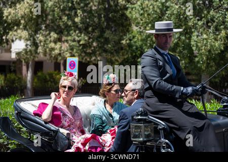 Sevilla, Espagne - 23 avril 23 : une charrue élégante tirée par des chevaux avec des gens élégamment habillés, mettant en vedette un homme en tenue formelle de conduite, et deux femmes en c. Banque D'Images