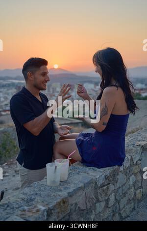 Couple jouant des ciseaux de papier de roche pendant le coucher du soleil Banque D'Images
