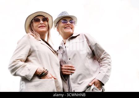 Deux femmes âgées élégantes dans des chapeaux d'été posent à l'extérieur, souriant contre le ciel lumineux avec espace de copie. Mode mature élégante, amitié et ag positif Banque D'Images