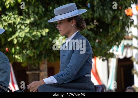 Sevilla, Espagne - 23 avril 23 : une jeune femme en tenue traditionnelle à cheval, portant un costume gris et un chapeau à larges bords, avec une expression ciblée, Banque D'Images