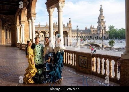 Sevilla, Espagne - 23 avril 23 : quatre femmes en robes de flamenco traditionnelles posent sur une belle place avec des arches et un bâtiment historique en arrière-plan Banque D'Images