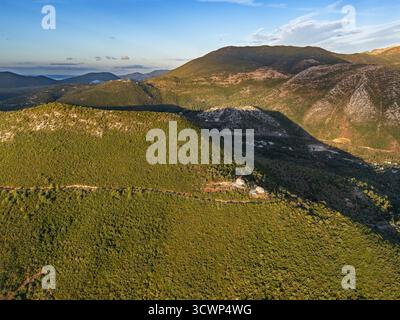 Vue aérienne des collines ondulantes couvertes de feuillage verdoyant, attrapant la lueur chaude du soleil couchant, créant une tapisserie de lumière et d'ombre, Desimi, Lefkada, Grèce. Banque D'Images