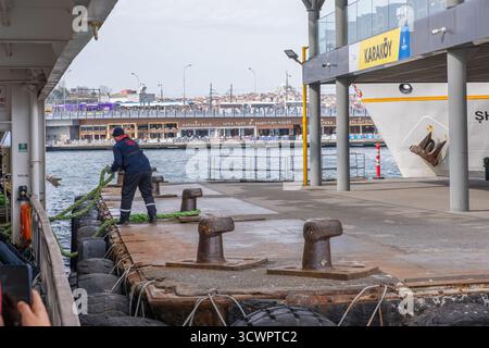 Istanbul, Turquie - 10 mars 2023 : Karakoy ferry fock avec un travailleur amarrant un navire à l'aide de cordes épaisses sur le quai rouillé. Les gens attendent le ferry Banque D'Images