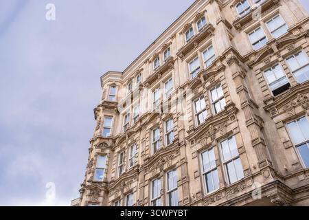 Immeuble historique, élégant et à plusieurs étages avec façade ornée et grandes fenêtres, installé dans un ciel nuageux. Vintage, urbain, vieux bâtiment Banque D'Images