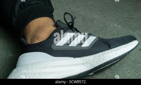 South Kalimantan, Indonésie - 11 24 2024 : Noir et blanc Adidas chaussures pureboost porté sur les pieds sur un fond gris Banque D'Images