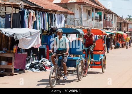 Miandrivazo, Madagascar - 11 octobre 2025 : trajet quotidien à Miandrivazo, montrant les rickshaws à cycle brillamment couverts utilisés pour le transport de passagers. Banque D'Images