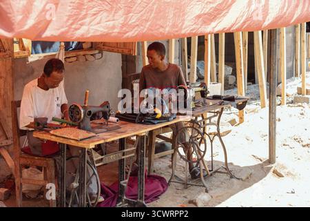 Miandrivazo, Madagascar - 11 octobre 2025 : tailleurs locaux travaillant sur des machines à coudre vintage dans un atelier extérieur improvisé à Miandrivazo. Banque D'Images