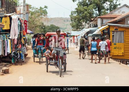 Miandrivazo, Madagascar - 11 octobre 2025 : trajet quotidien à Miandrivazo, montrant les rickshaws à cycle brillamment couverts utilisés pour le transport de passagers. Banque D'Images