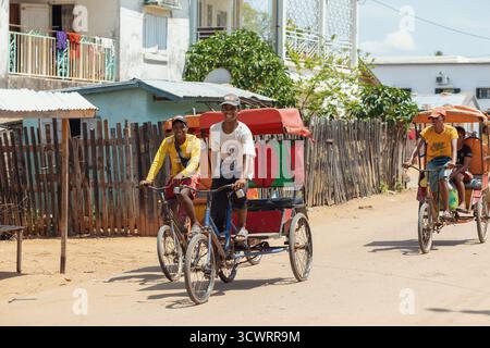Miandrivazo, Madagascar - 11 octobre 2025 : trajet quotidien à Miandrivazo, montrant les rickshaws à cycle brillamment couverts utilisés pour le transport de passagers. Banque D'Images
