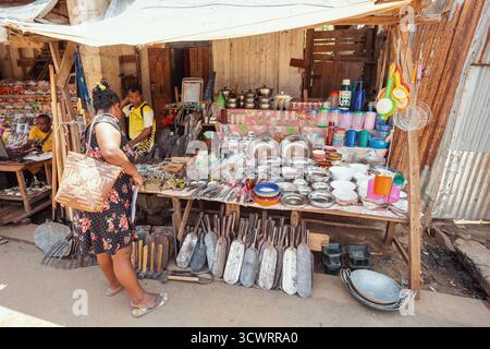 Miandrivazo, Madagascar - 11 octobre 2025 : femme locale faisant du shopping dans un étal de rue vendant des ustensiles de cuisine et des outils agricoles sur le marché de Miandrivazo Banque D'Images