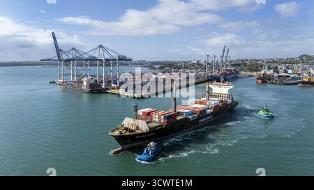 Auckland, Nouvelle-Zélande - 19 septembre 2025 : vue aérienne d'un porte-conteneurs, éclipsé par les grues et une mer de conteneurs au port, contraste avec les eaux turquoises du port. Banque D'Images