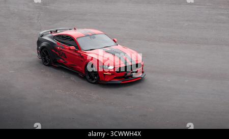 Red Ford Mustang dans le parking au crépuscule. Vue aérienne de trois quarts de face d'un poney américain garé sur un immense champ d'asphalte vide. Banque D'Images