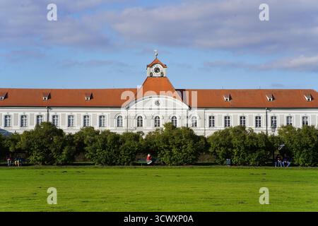 Aile latérale du palais de Nymphenburg à Munich, Allemagne, avec toit en tuiles rouges, façade baroque blanche et parc vert ouvert au premier plan.Palais de Nymphenburg Banque D'Images