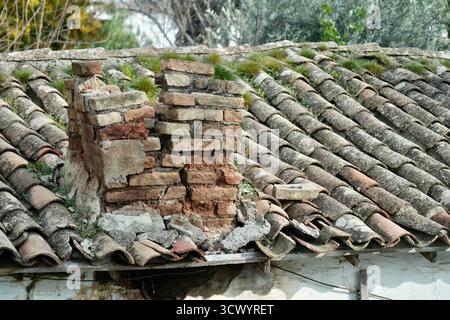 Une cheminée rustique en brique effondrante sur un toit en tuiles. Banque D'Images