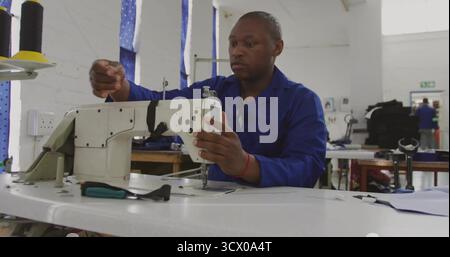 Machine à coudre industrielle en fonctionnement, homme portant un filetage uniforme bleu en atelier, avec des bobines Banque D'Images