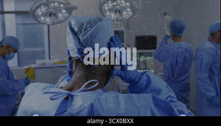 Mise en place d'une casquette chirurgicale au milieu d'un chirurgien adulte masculin dans la salle d'opération, avec superposition numérique et moniteurs Banque D'Images
