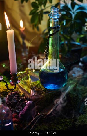 la potion bleue se trouve dans une bouteille en verre sur une table couverte de mousse. Les bougies scintillantes diffusent une lueur chaude, tandis que les plantes ajoutent à l'atmosphère enchanteresse de la Banque D'Images