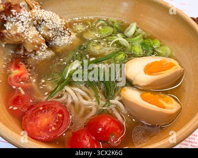 Gros plan un bol de ramen avec oeuf, tomates et poulet au sésame sur des brochettes. Bouillon chaud, culture gastronomique japonaise et harmonie culinaire à travers la texture Banque D'Images