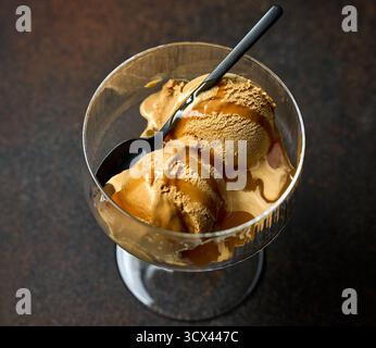 cuillère à crème glacée au caramel avec sauce servie dans un verre sur fond de table brun foncé Banque D'Images