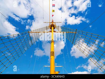 Prise en plein jour dans un port japonais d'Osaka, cette vue en bas angle du mât d'un navire jaune avec des drapeaux de signalisation et des filets grimpants évoque la publicité maritime Banque D'Images