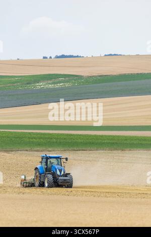 Tracteur bleu cultivant un sol sec dans un paysage rural sous un ciel dégagé Banque D'Images