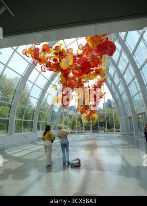 SEATTLE - APR 25, 2025 - deux femmes regardent une grande sculpture en verre coloré de Dale Chihuly suspendue au plafond d'un moderne et lumineux Banque D'Images