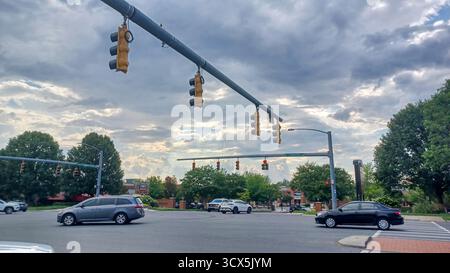 Charlotte, NC, États-Unis - 2 octobre 2025 : des feux de circulation pendent au-dessus d'un carrefour de route achalandée avec des voitures qui passent par un jour nuageux. Banque D'Images
